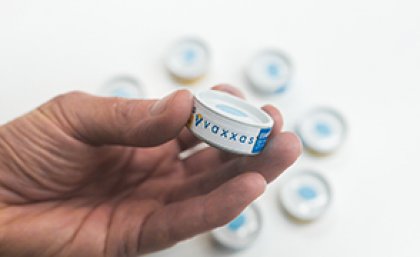 A hand holding a cannister containing the vaccine patch.